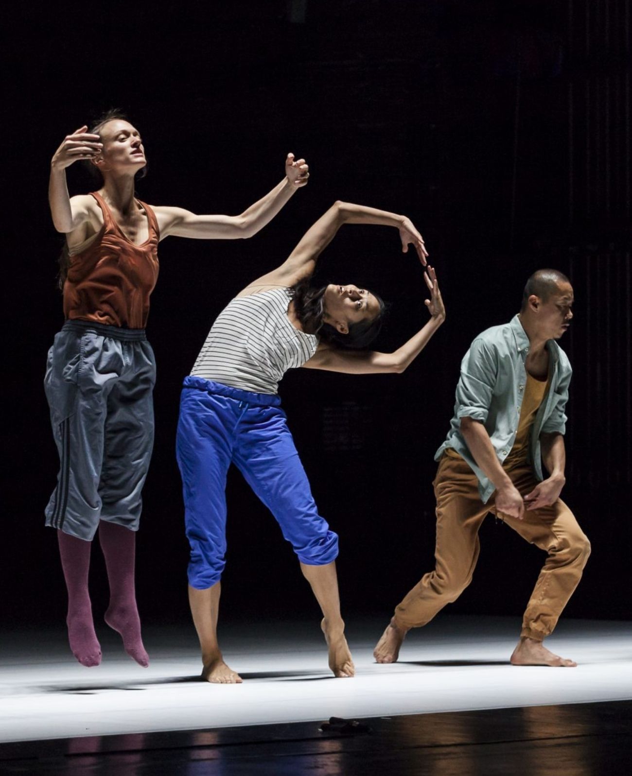 Three performers stand in a line each forming different shapes with arms outstretched