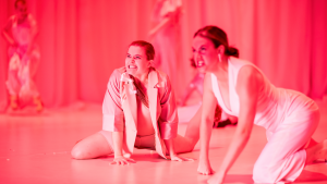Bathed in bright pink light, two dancers crouch low to the ground and bare their teeth